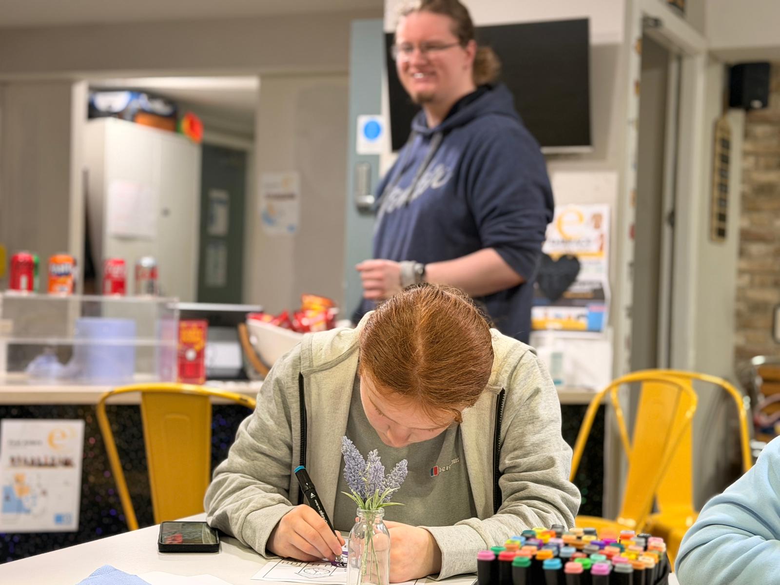one young person working with another person behind them smiling